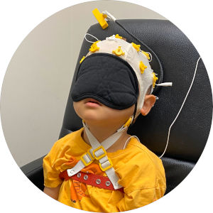 아이가 의자에 앉아서 안대를 쓰고 뇌파측정기를 머리에 쓰고 뇌파와 심전도를 측정하는 모습